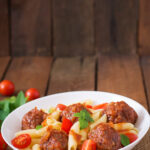 Penne pasta with meatballs in tomato sauce in a white bowl